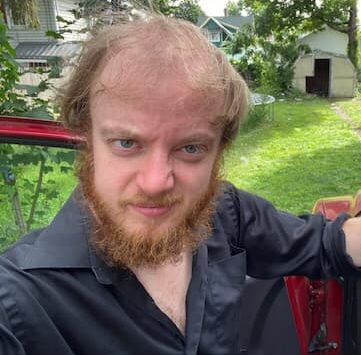 smiling selfie of a bearded luke wenke standing outside his red suv in 2023