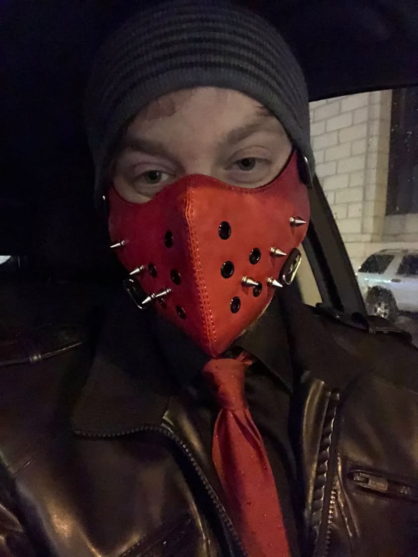 Luke Wenke wearing a red spiked face mask, black beanie, leather jacket, and red tie.