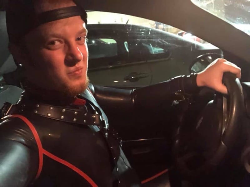 a selfie of luke wenke sitting in the driver's seat of his car in a bdsm gimp suit